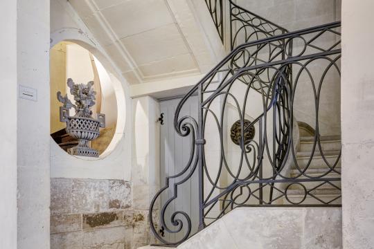 Grand escalier en pierre et rampe en fer forgé.